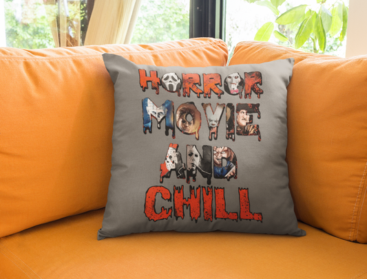 greay pillow on a leather couch. The pillow reads horror movie and chill and has faces of killers from horror movies in the words